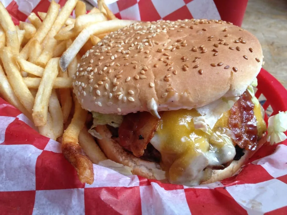 A cheeseburger with bacon and a pile of fries in a red checked basket