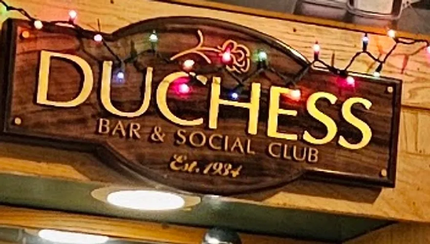 The carved wooden sign behind the bar reading Duchess Bar and Social Club, Est. 1934