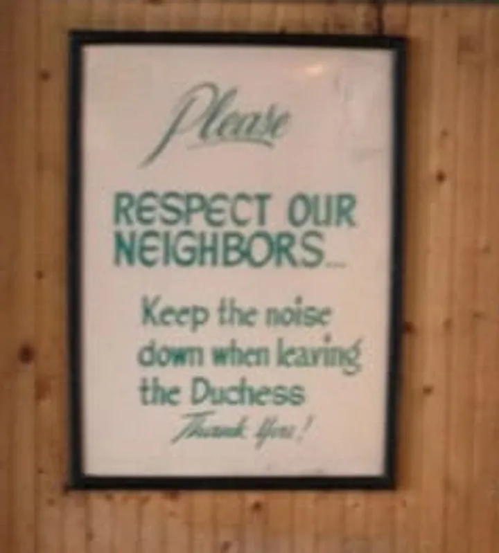A framed sign on the wood panelling by the door reading: Please respect our neighbors. Keep the noise down when leaving the Duchess. Thank you.