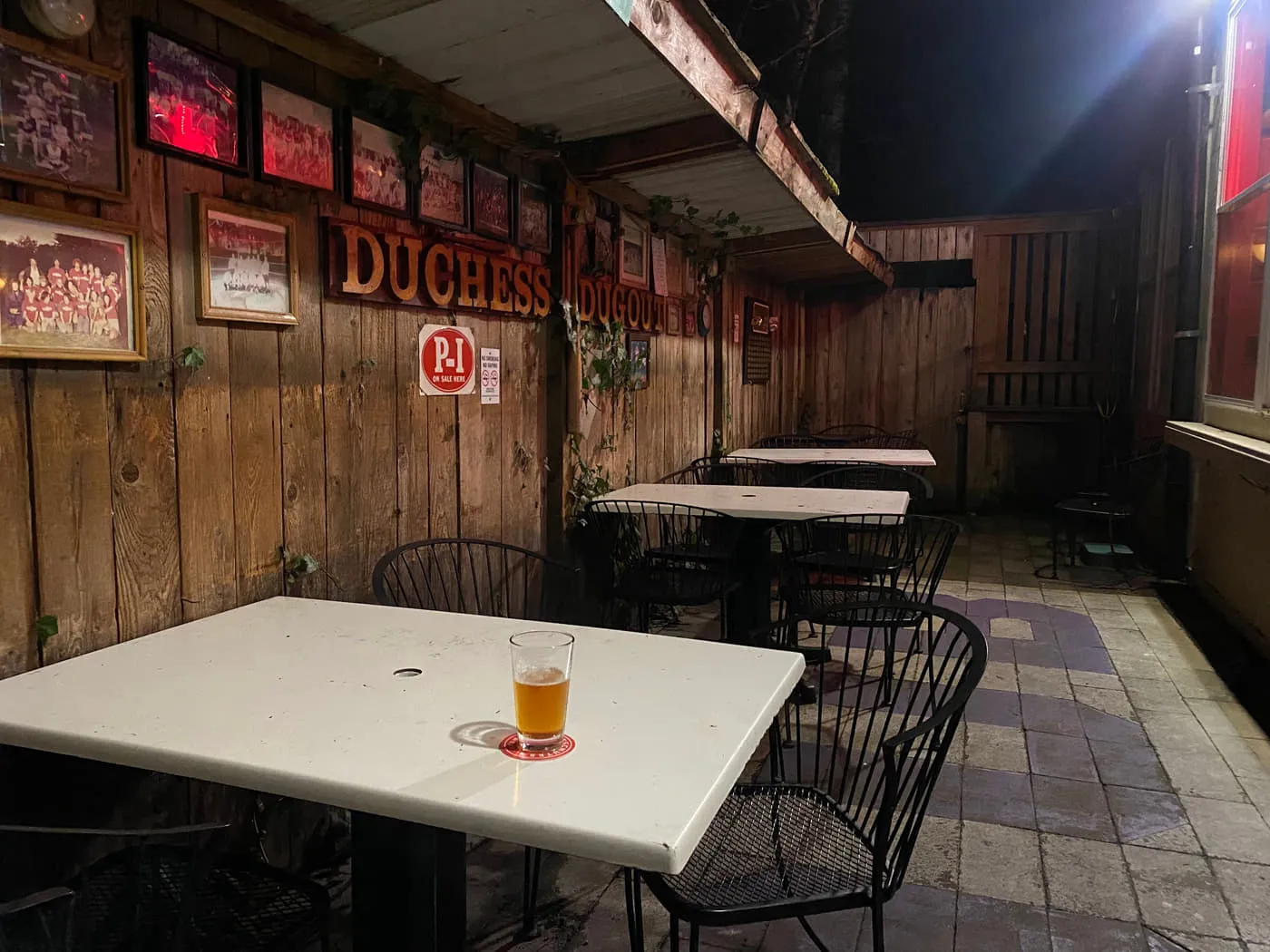 The covered back patio at the Duchess Tavern with cedar walls, a Duchess sign and metal tables