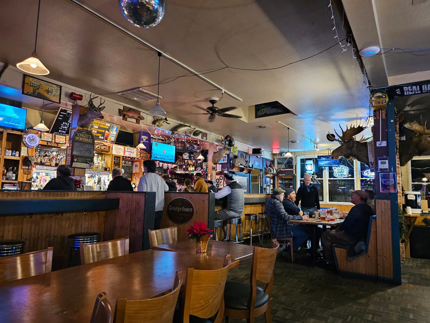 The front room of the Duchess Tavern with people at the bar and in the booths, a mirror ball, mounted moose and televisions
