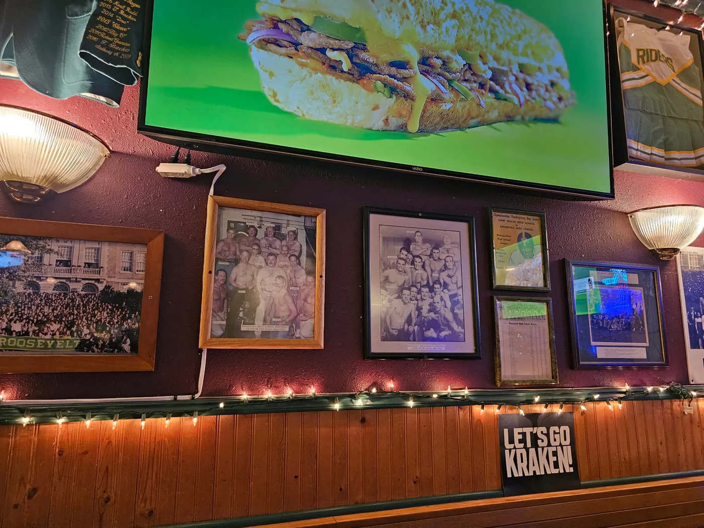 A wall at the Duchess covered in framed photographs of old Seattle and Husky teams, with string lights along the wainscot