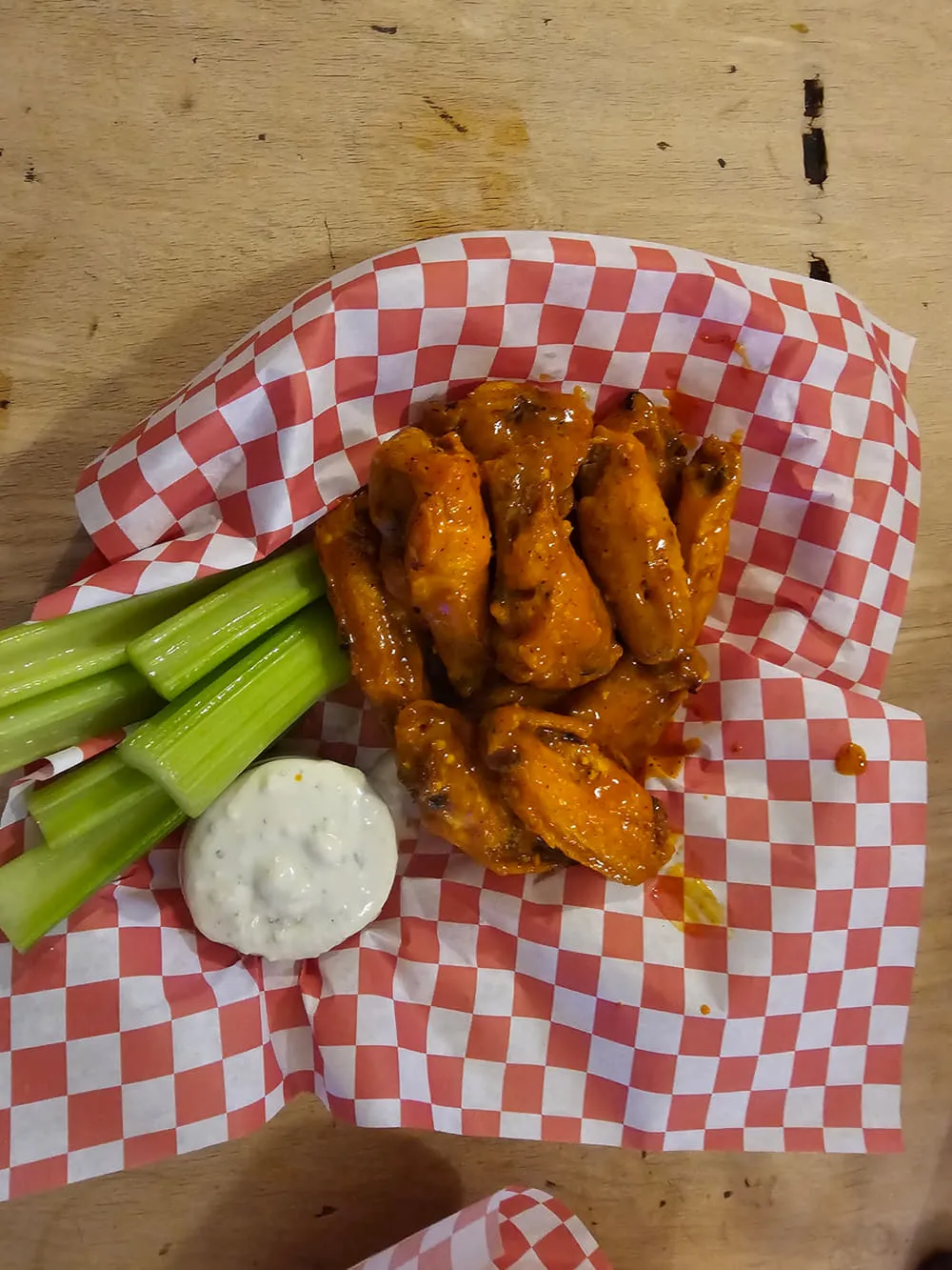 Buffalo wings with celery sticks and ranch in a red checked basket